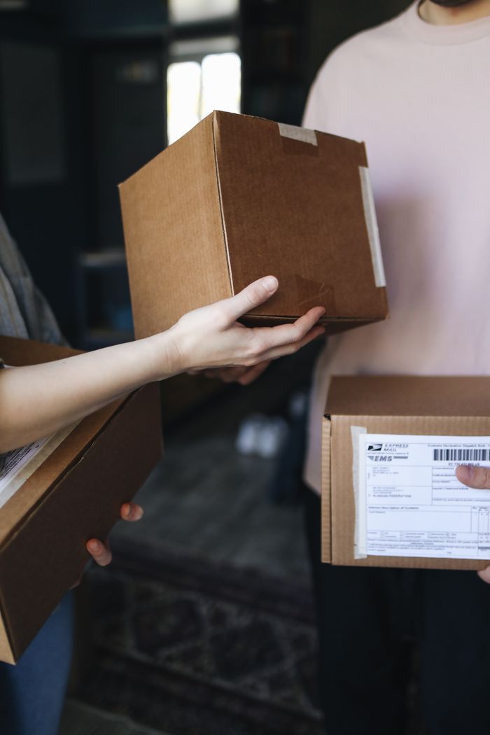 Close-up of hands exchanging cardboard delivery packages indoors.