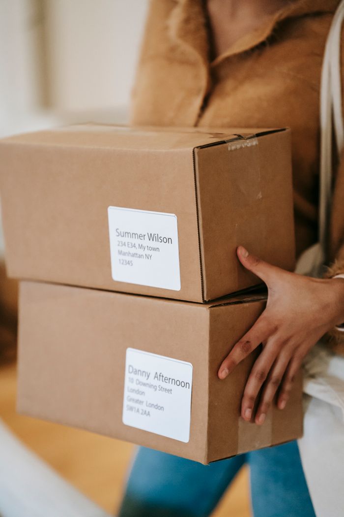 Crop anonymous female in casual clothes bringing carton parcels with address labels in post office
