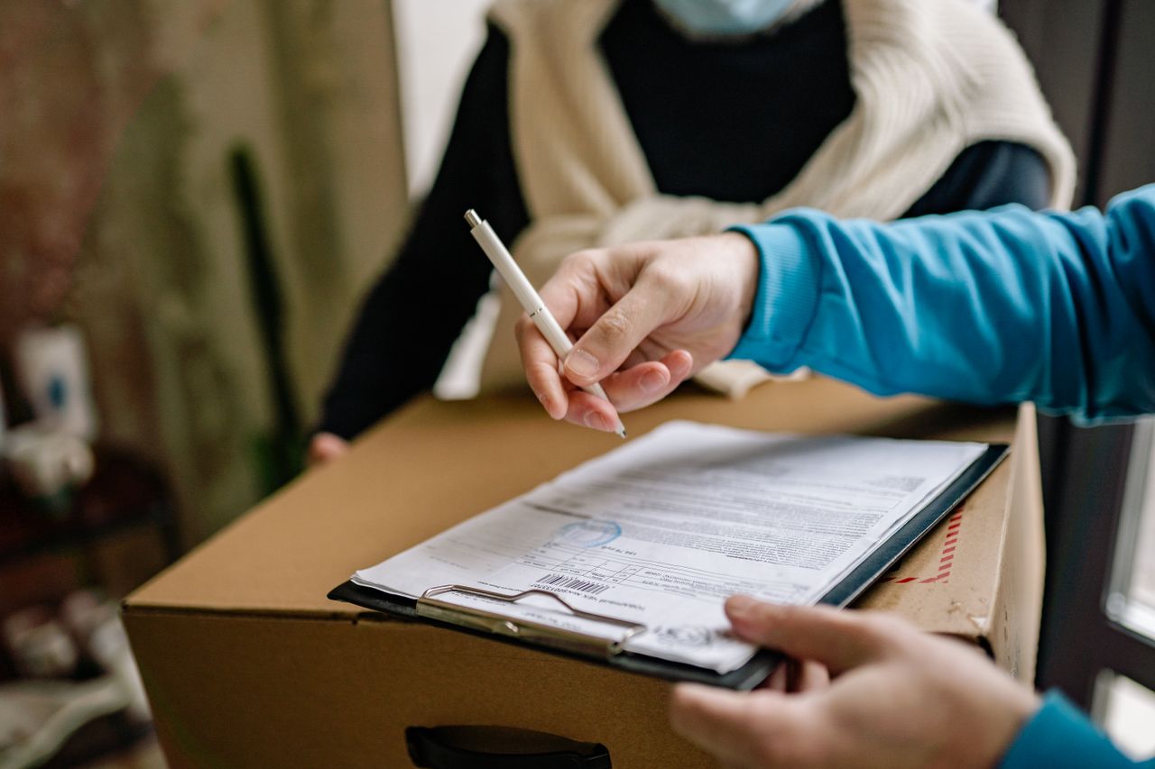 Home Close-up of a person signing a delivery document placed on a large cardboard box indoors.